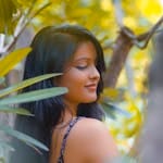 A serene portrait of a woman amidst lush green foliage in daylight.