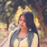 Portrait of an elegant South Asian woman in a stylish yellow dress and scarf, captured outdoors in natural light.